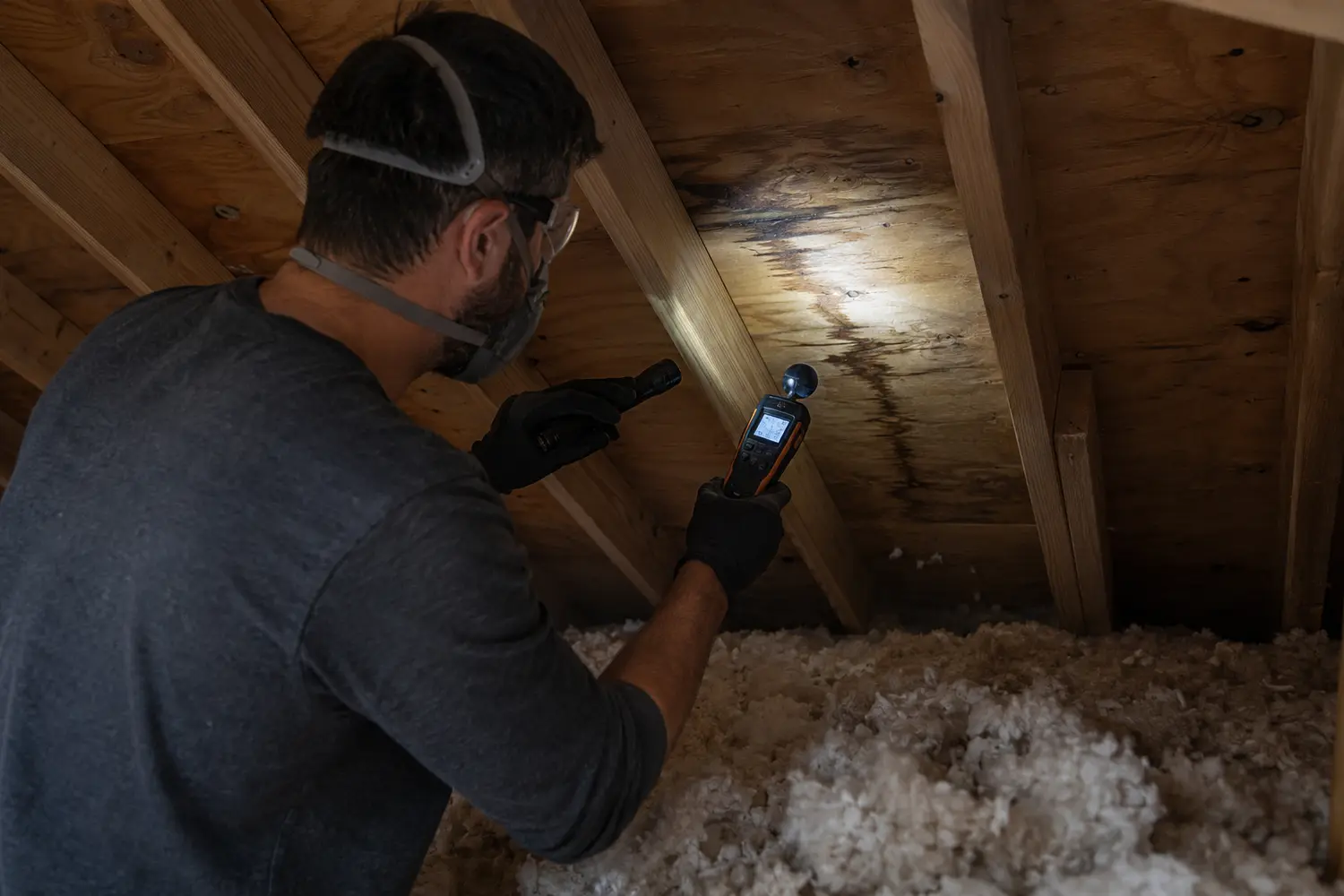 Professional roofer inspecting a residential attic with a flashlight, tracing the source of a leak